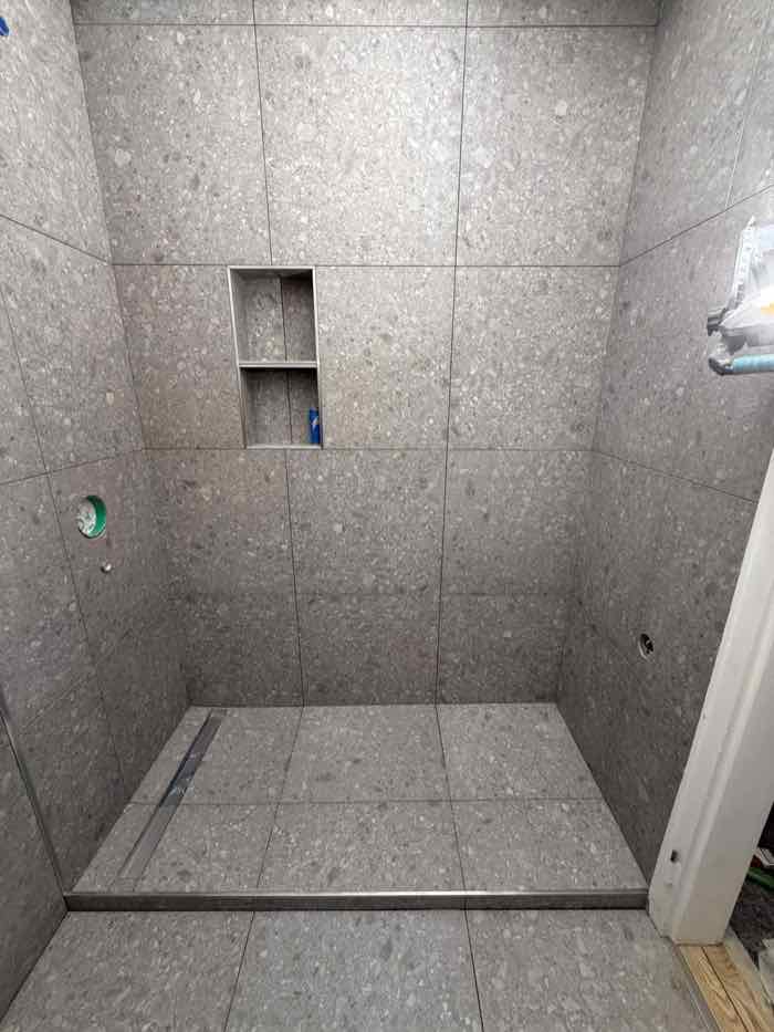 Bodengleiche Dusche in grauer Terrazzo-Optik mit zweigeteilter Wandnische und Linienentwässerung