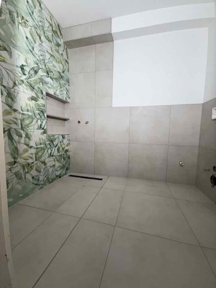 Dusche mit Dekorwand im grünen Blattmuster neben hellgrauen Großformatfliesen