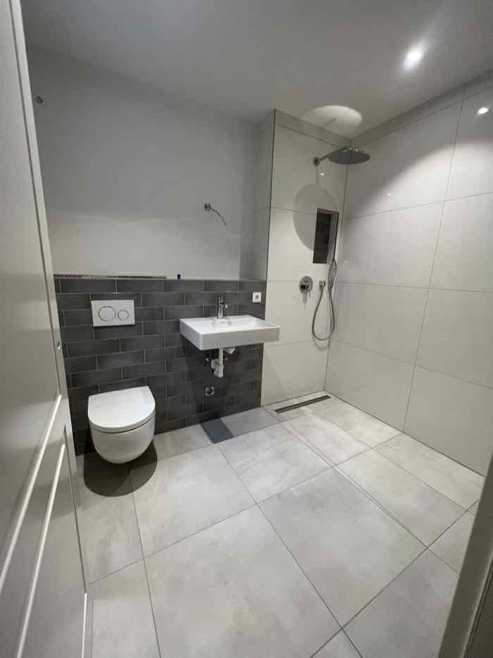 Fertiges Badezimmer mit dunkler Riemchenwand, Wandwaschtisch und bodengleicher Regendusche