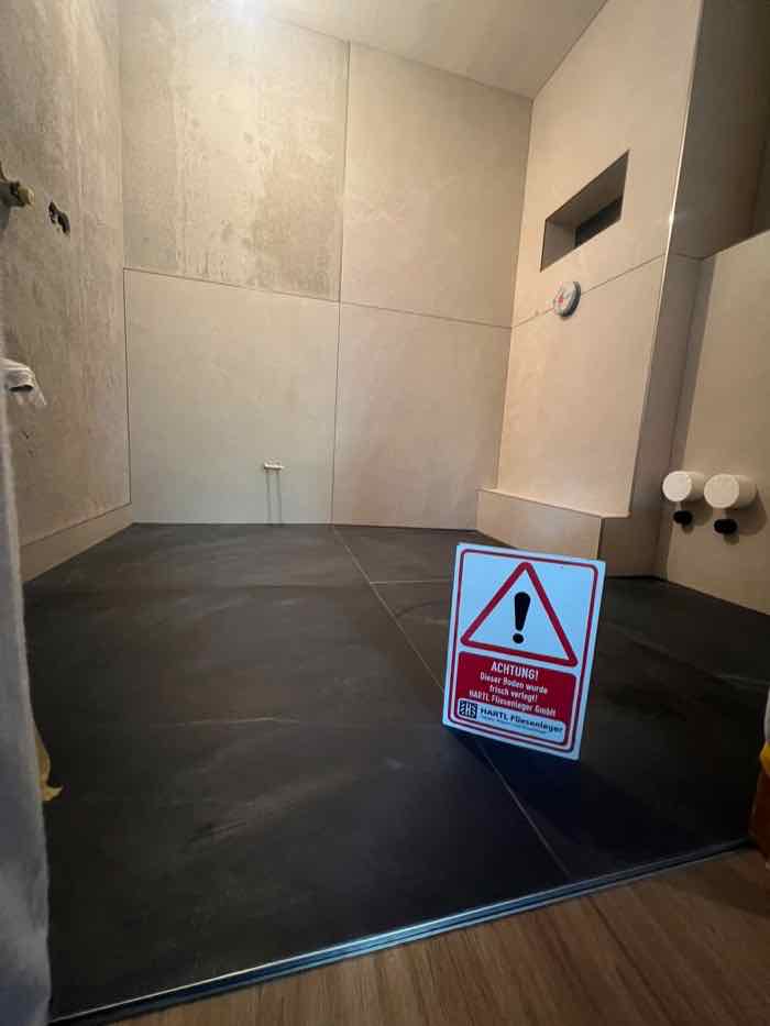 Duschbereich in Travertinoptik mit eingelassener Nische und anthrazitfarbenem Boden