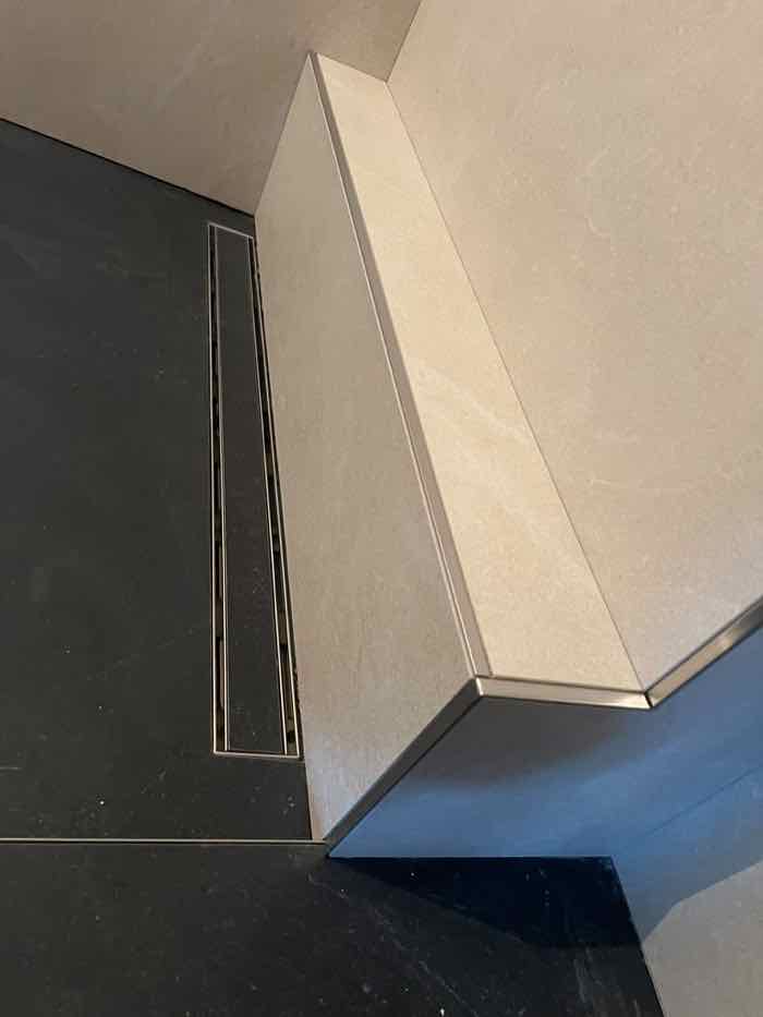 Gehrungsgeschnittene Kante einer verfliesten Sitzbank neben einer Edelstahl-Duschrinne