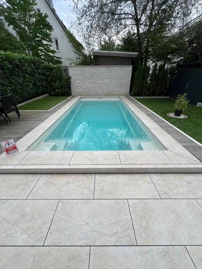 Gartenpool mit umlaufender Beckenrandeinfassung und Terrassenplatten in Steinoptik